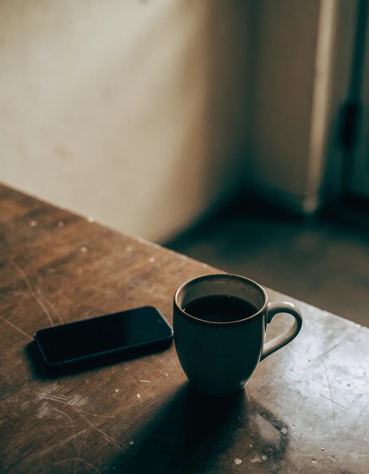 A phone lying face down beside a half-finished mug on a kitchen table